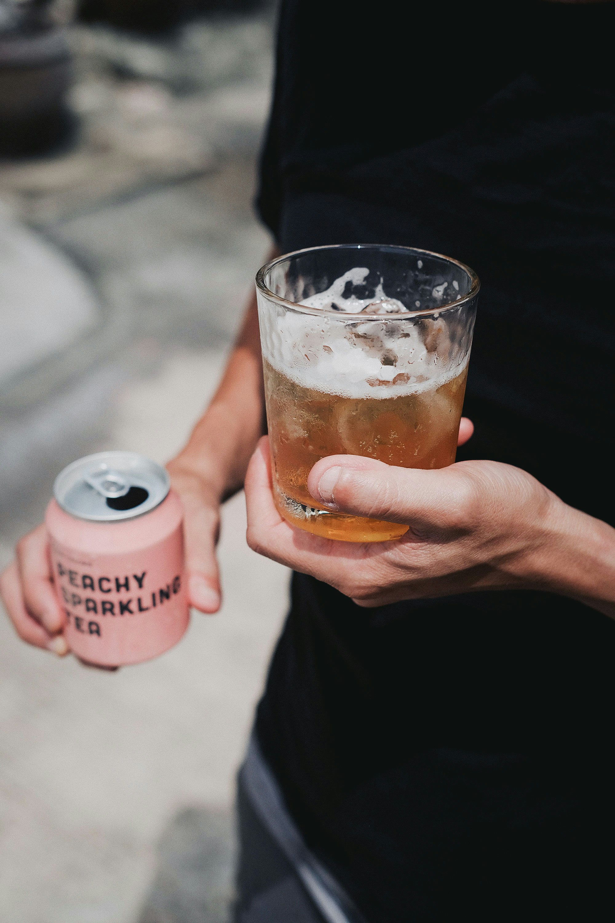 person holding clear drinking glass with brown liquid